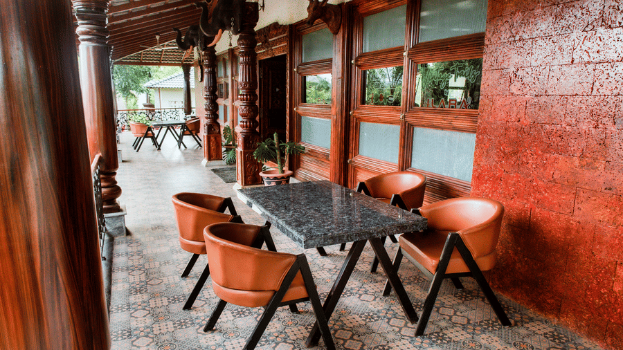 A covered outdoor seating corridor with a rectangular table, 4 brown chairs, and large windows | Vintage Trails By Ilara