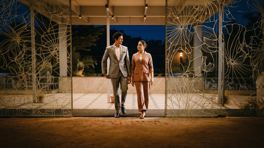 Two guests walking through the lotus-etched glass entrance doors of Ilara Hotels & Spa, Tada, beneath a lit porch with columns at dusk.