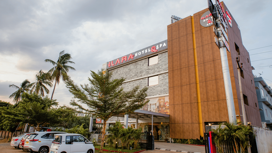 Front facade with stone cladding, an entrance canopy, landscaped trees and a pylon sign listing the outlets of Ilara Hotels & Spa, Tada.