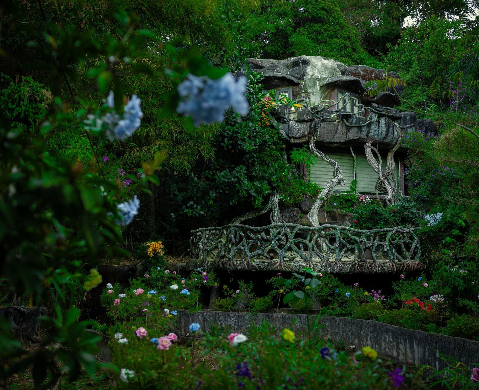 An image of a cave room amidst the jungle with pretty flowers and shurbs