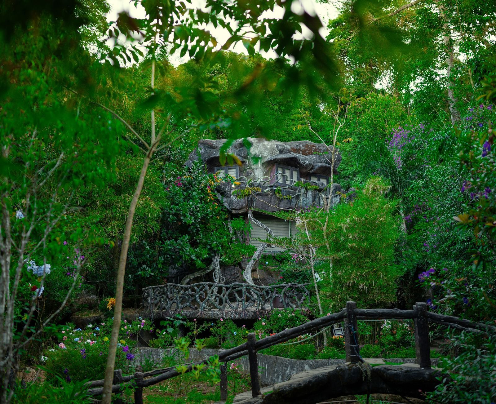 An image of a facade set amidst the forest and there's also a bamboo bridge  in front of the facade - Parakkat hotel & resorts