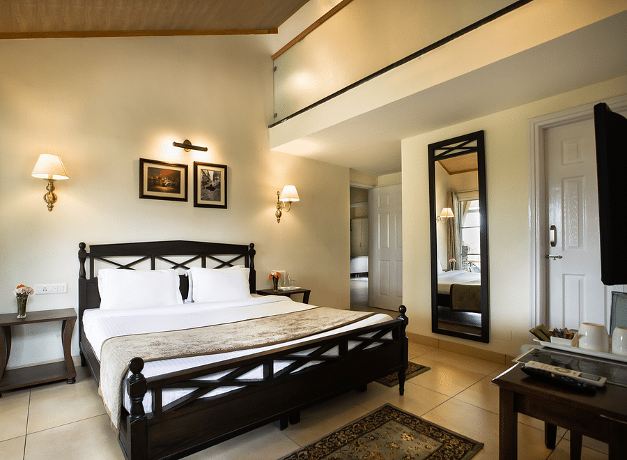 A luxurious room with a king size premium bed with soothing white coloured walls and a wall mirror on the right - Lamrin Norwood Green, Palampur