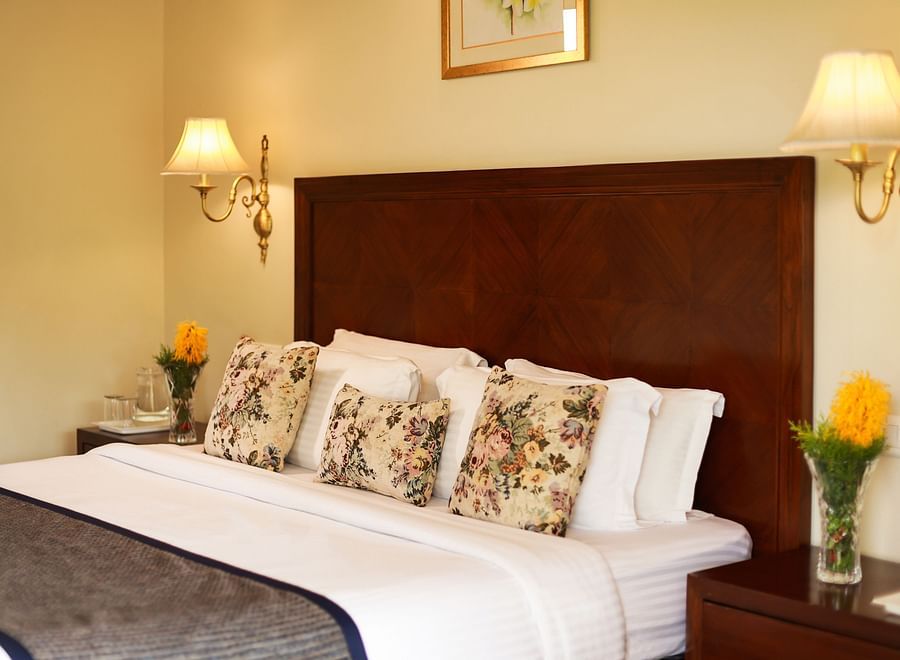 alt-text Closer view of a beautifully tucked bed with soft lines and pillows along with bedside lamps - Lamrin Norwood Green, Palampur