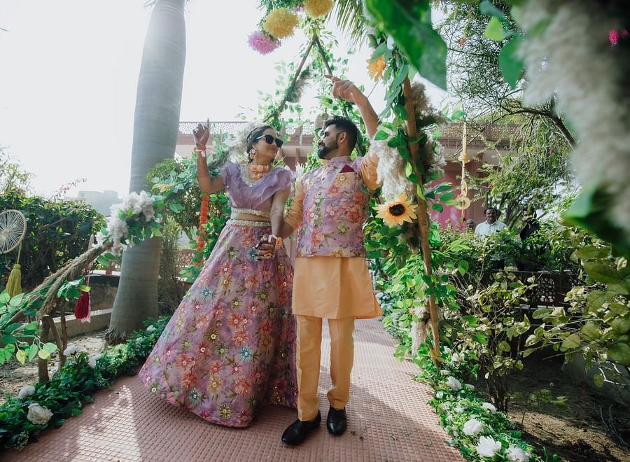 Bride and groom holding hands and walking down a garden pathway under lush green foliage.