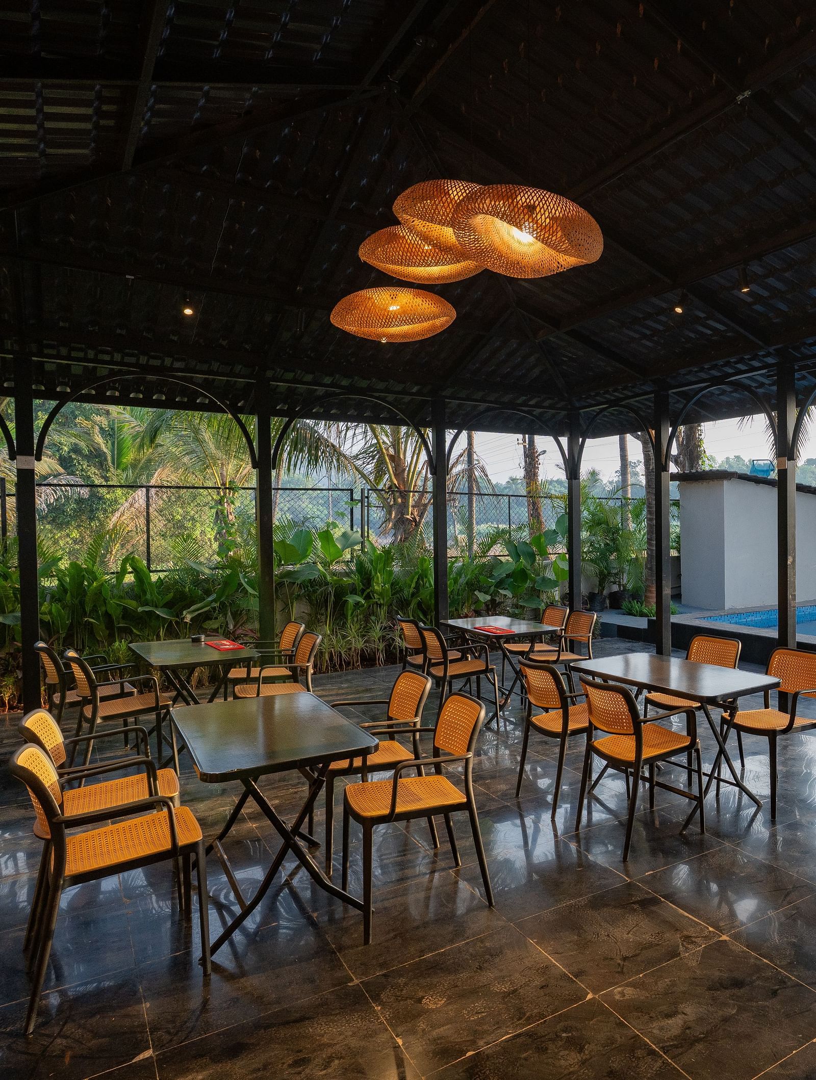 Covered open-air dining area with tables and chairs, overlooking a swimming pool and lush greenery at Kssemya.