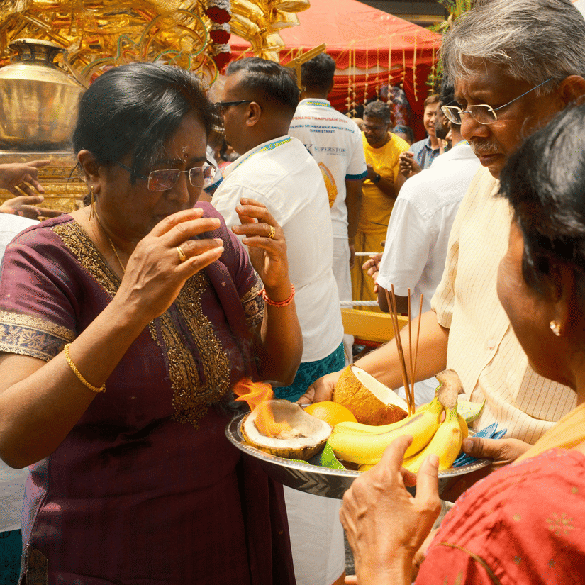 People are gathered around a temple to take aarthi from a woman.