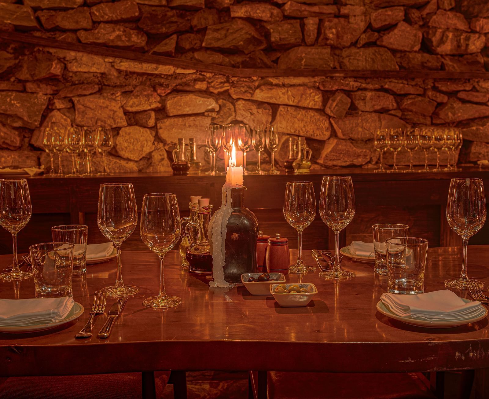 Elegant candlelit dining table set with wine glasses and dinnerware, in a rustic stone-walled room.
