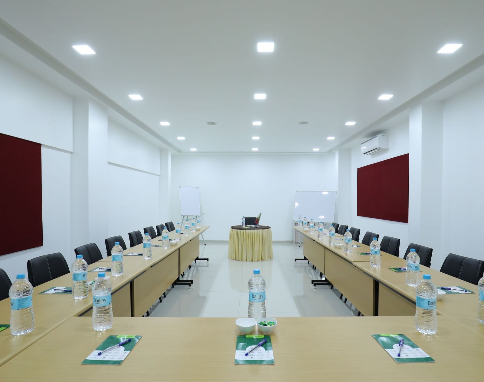 A meeting room at Imperial Grande with various tables and chairs arranged in a U-shape, featuring red soft boards on the wall.