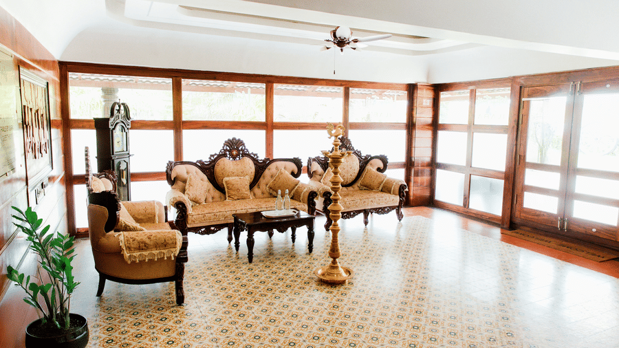 An indoor lounge or lobby area with decorative floor tiles, wood-panelled glass walls, and a classic beige sofa set | Vintage Trails By Ilara