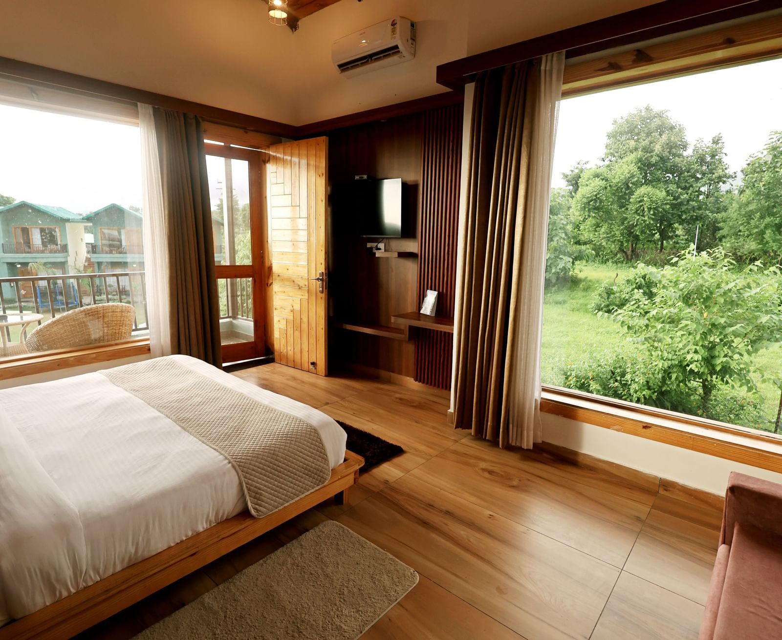 Spacious room with large windows and balcony offering lush greenery views at Corbett Nirvana Resort.