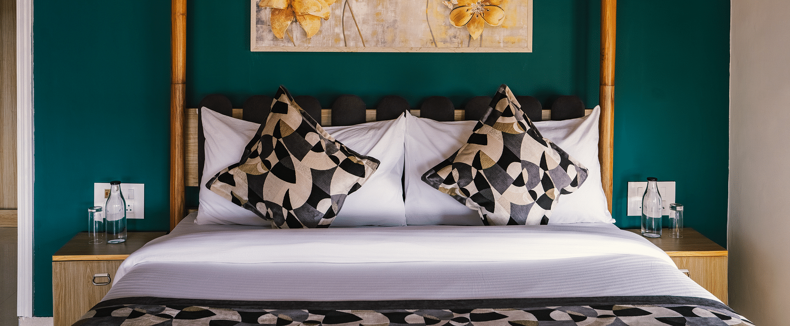 A neatly made bed with a photo frame above the headboard, a bedside table on each side, and a wooden frame at BluSalzz Villas - The Green Roof, Bhimtal.