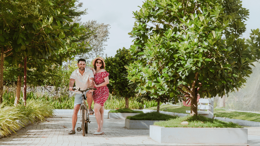 A man and a woman standing beside a bicycle on a paved outdoor pathway surrounded by green trees | Vintage Trails By Ilara