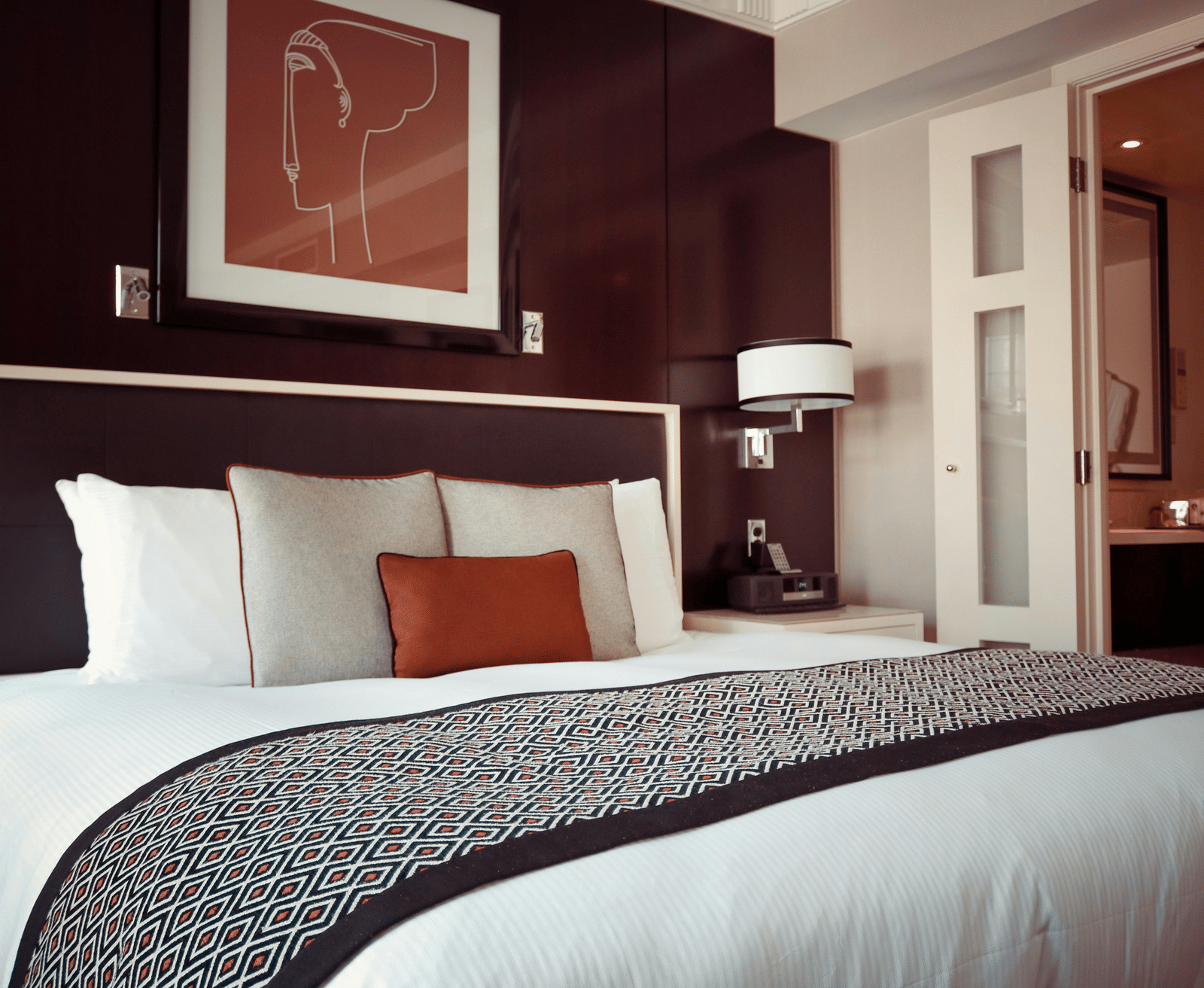 Modern hotel room with a large neatly made bed, stylish decor, and a view into the bathroom area.