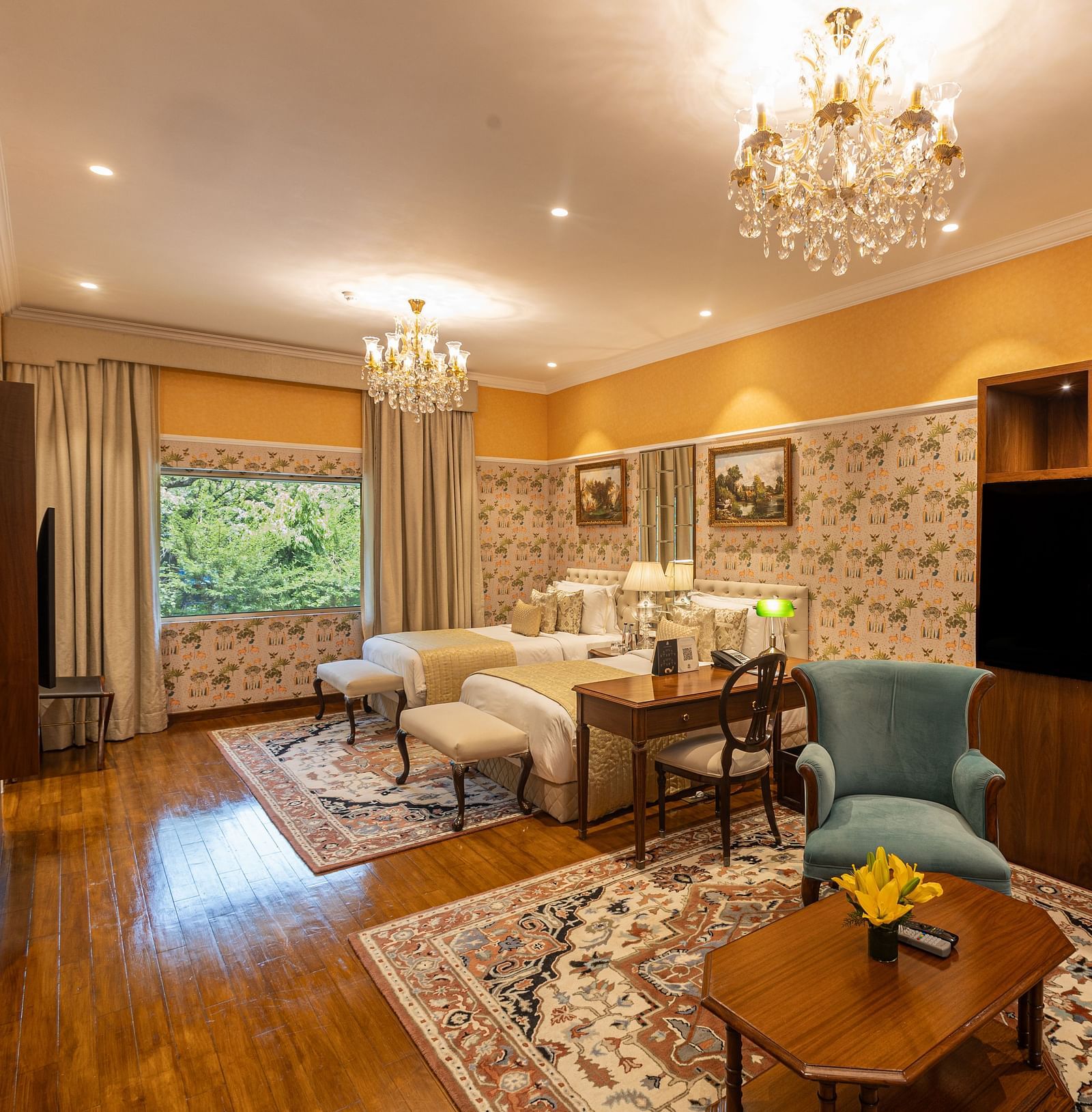 Grand Luxury Twin Bed Room at The Claridges New Delhi, featuring twin beds with chandeliers hanging above and a large glass window offering a scenic view