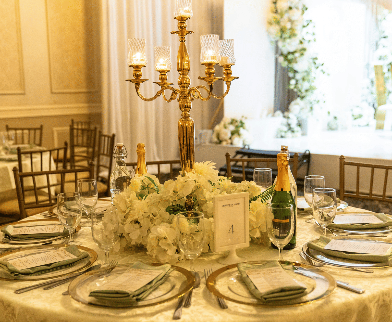 A formal dining table set for a wedding or event, featuring a large hydrangea centrepiece and a gold candelabra.