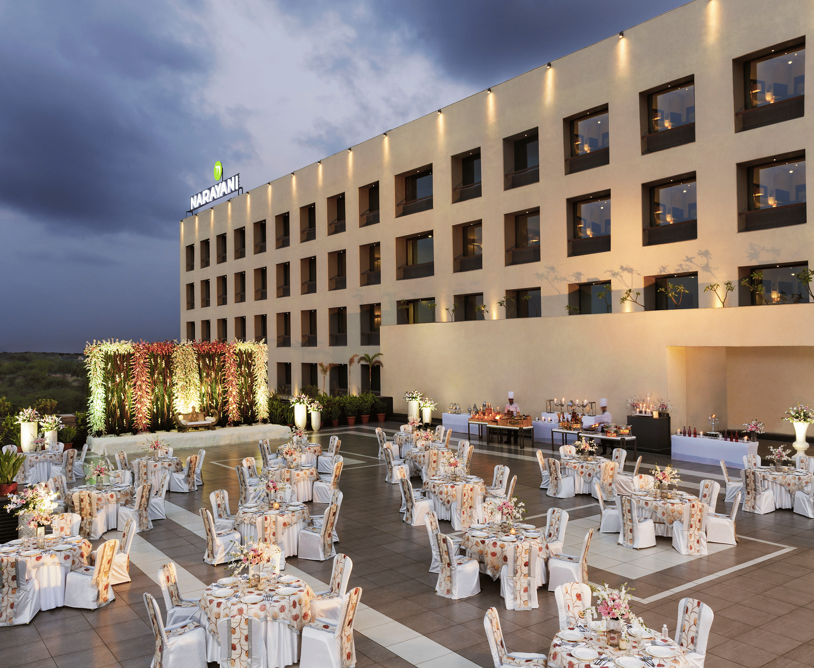 Outdoor banquet setup with white chairs and tables at Narayani Heights Hotel & Resorts, Ahmedabad.