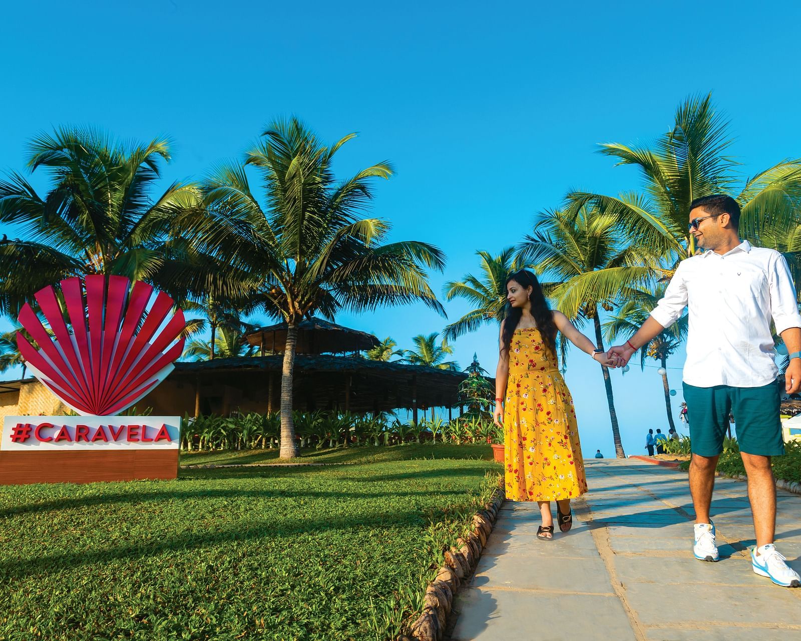 a couple walking holding hands next to Caravela Beach Resort Goa signage