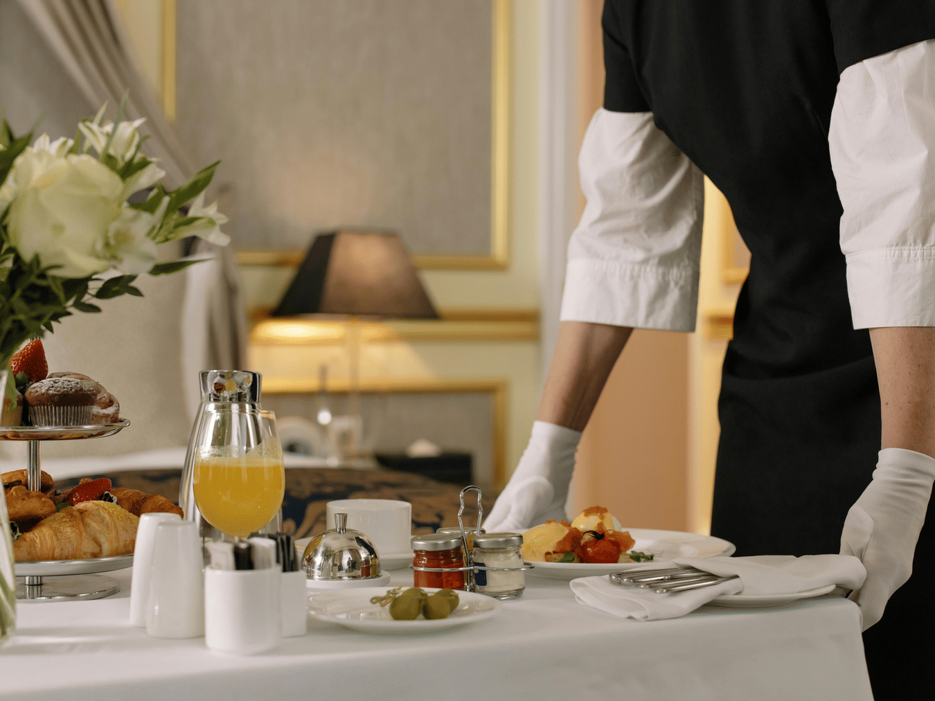 Server arranging breakfast with juice and fresh fruit on a dining table.