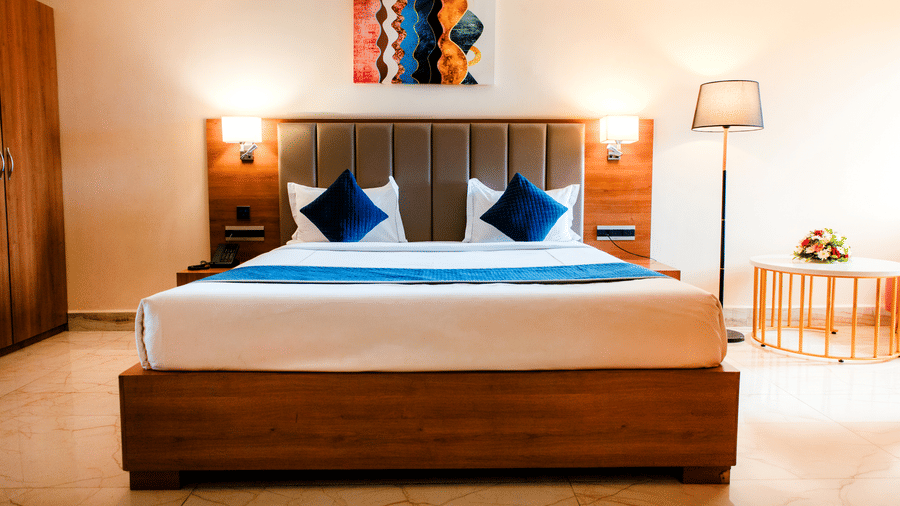 King bed in the Junior Suite with a padded headboard, teal cushions, quilted runner and bedside wall lamps at Ilara Hotels & Spa, Tada.