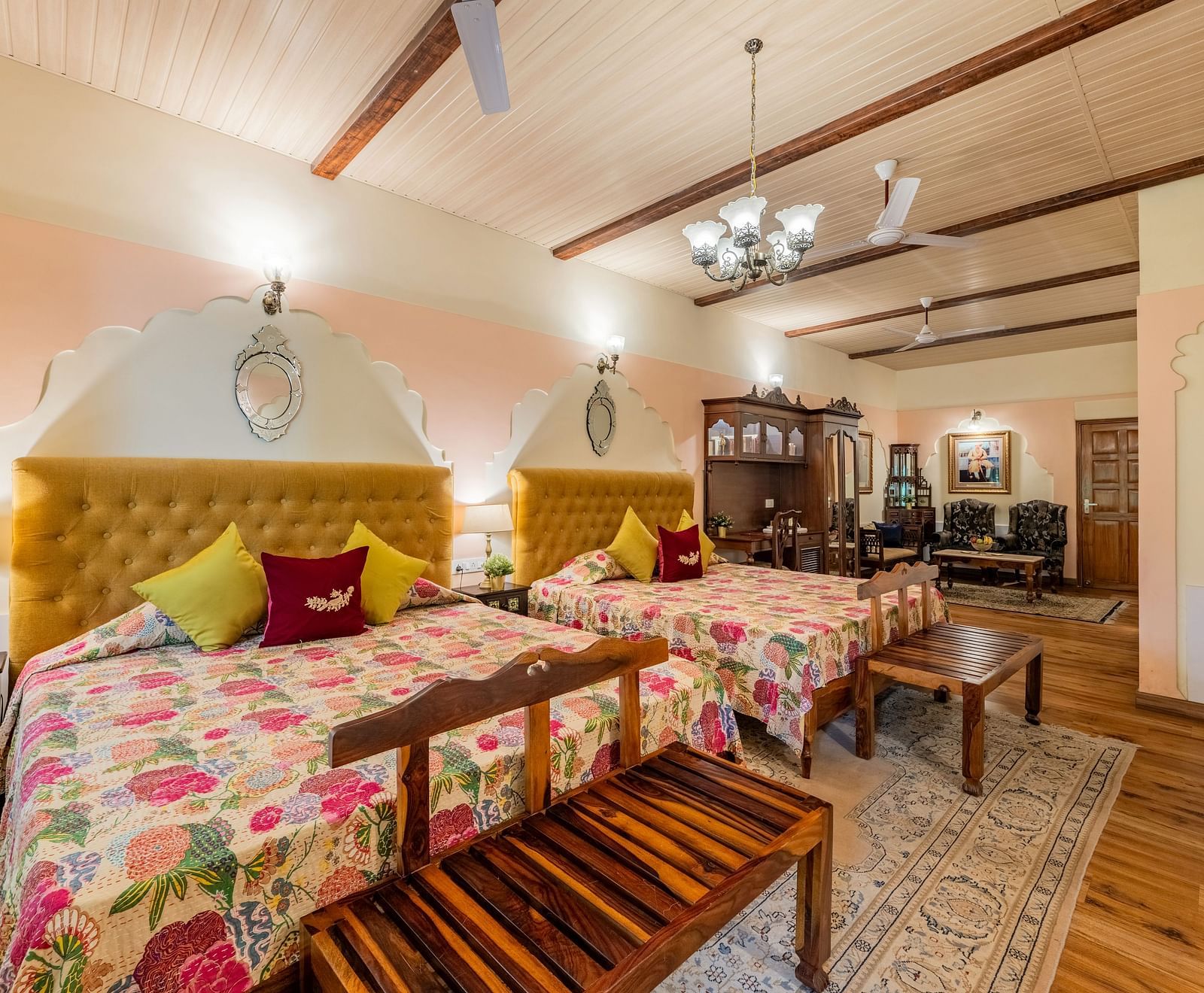 A bedroom with two beds, patterned bedspreads, yellow headboards, a chandelier, and a wooden bench | Dera Rawatsar, Jaipur