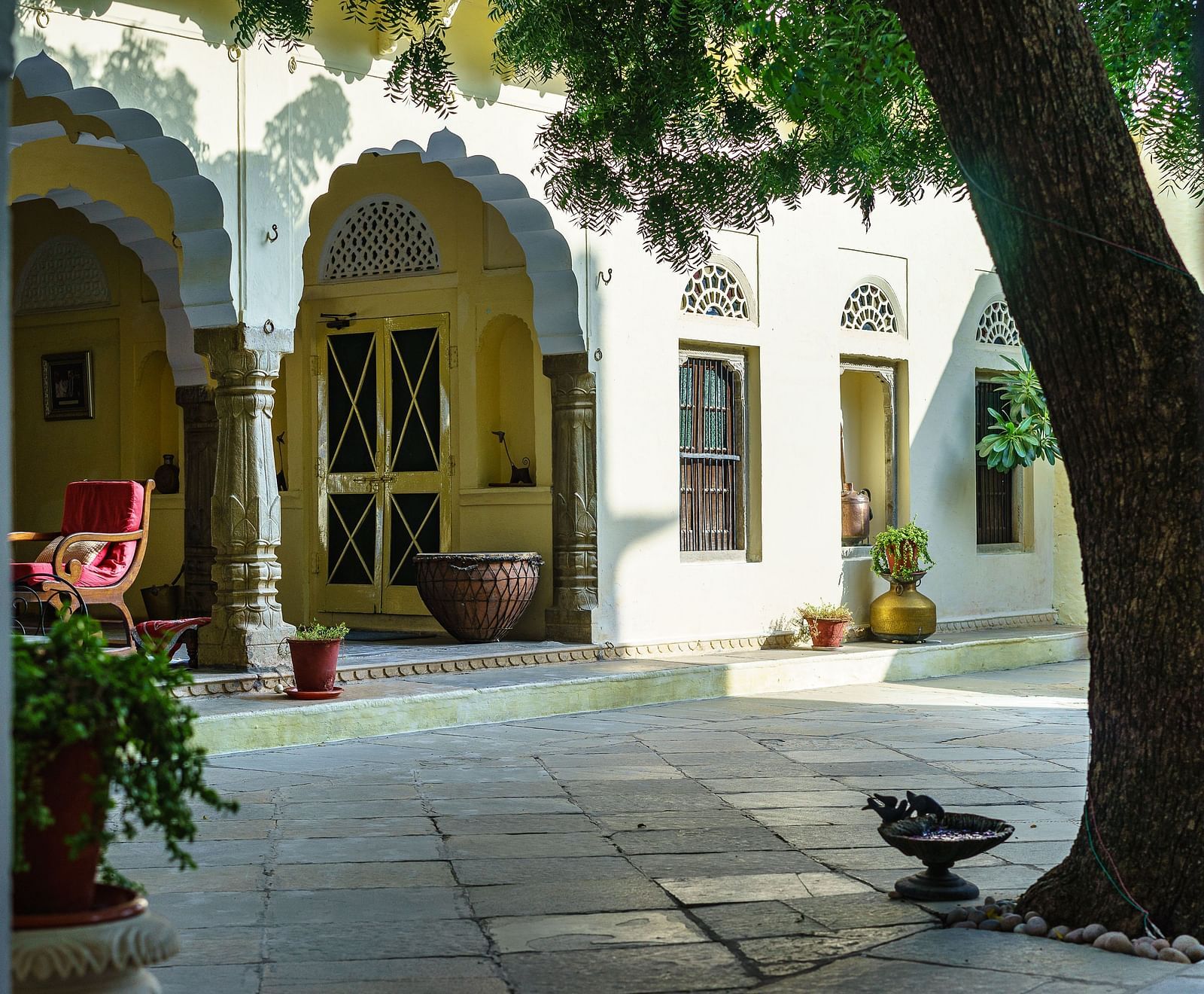 A serene courtyard at Fort Barli, with arched doorways and a large tree, captures the fort's tranquil atmosphere.