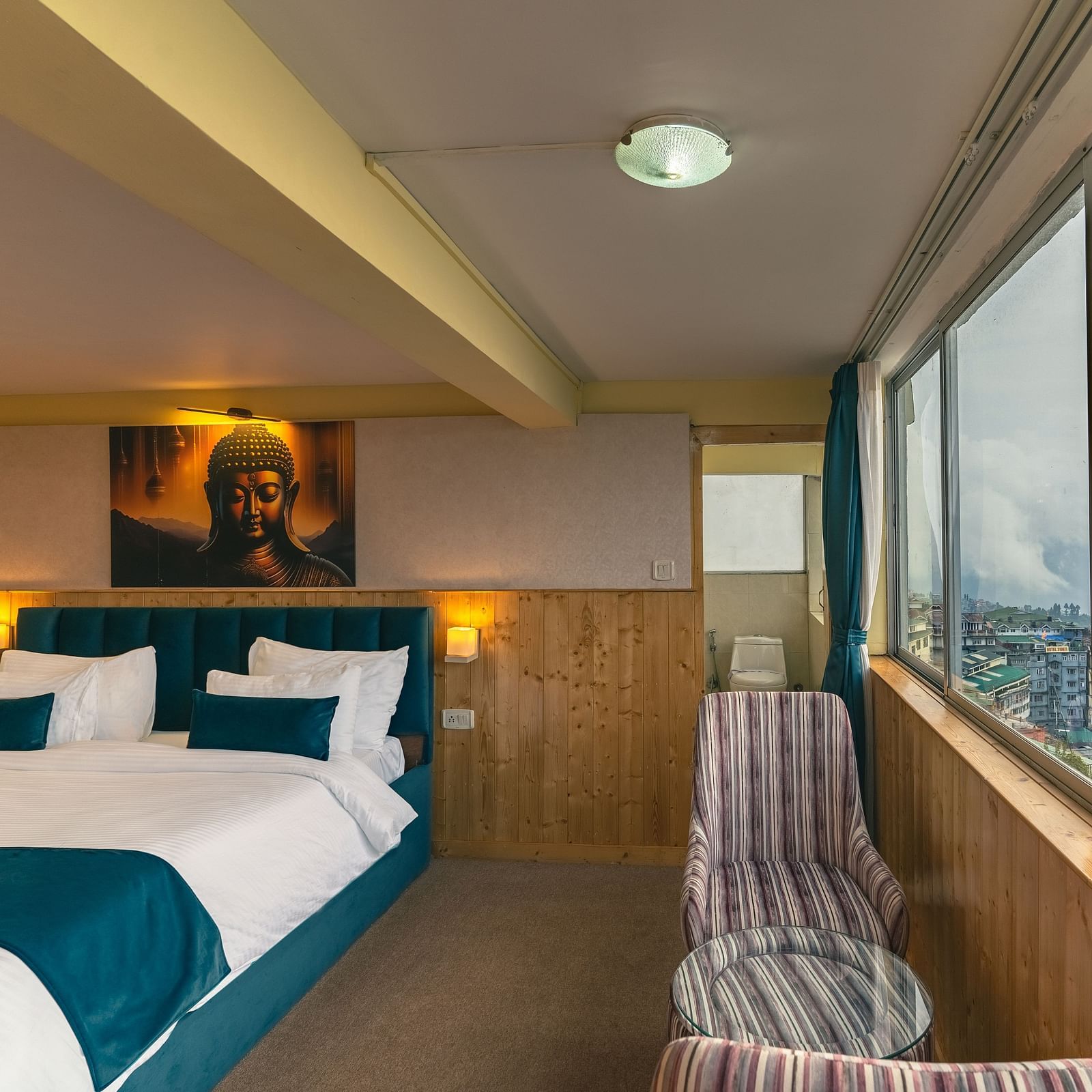 Suite with a king size bed, wall-mounted television, wooden table, and cosy lighting along with large window with city viewat Avianna Seven Seas, Darjeeling