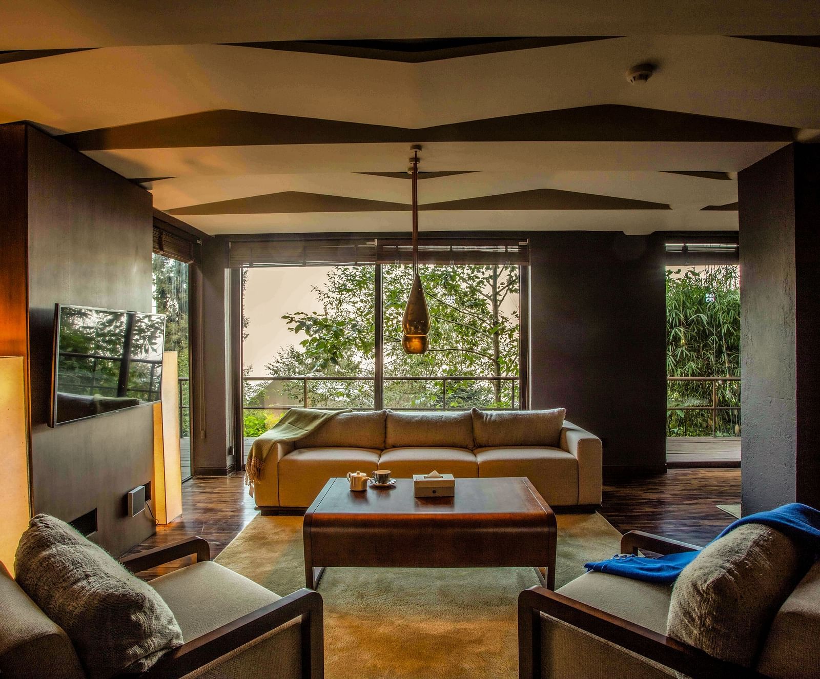 Spacious living room with modern decor, large windows offering a view of lush greenery.