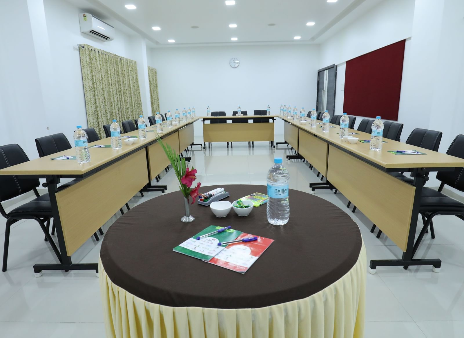 A conference room at Imperial Grande set up with a round table with additional amenities like bottled water and stationary, featuring chairs arranged in a U-shaped style.