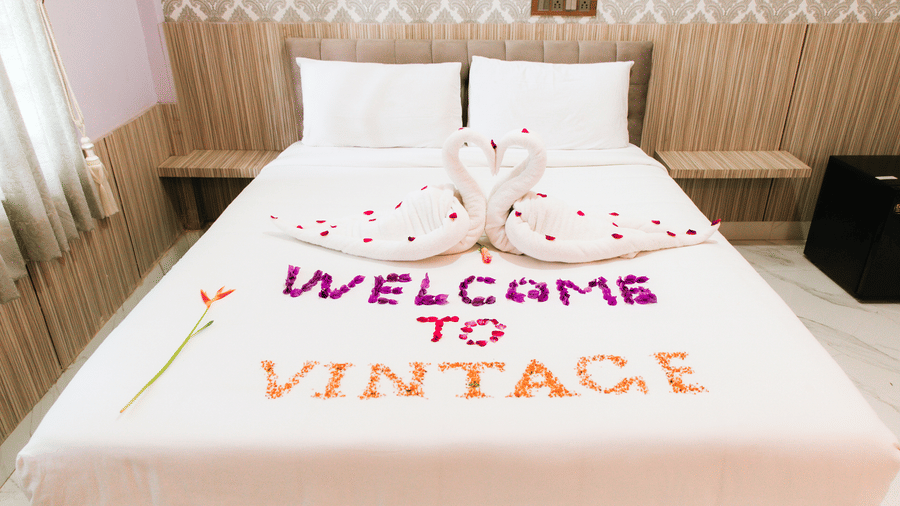 A double bed featuring white linen decorated with flower petals spelling out WELCOME TO VINTAGE and towel swans | Vintage Trails By Ilara