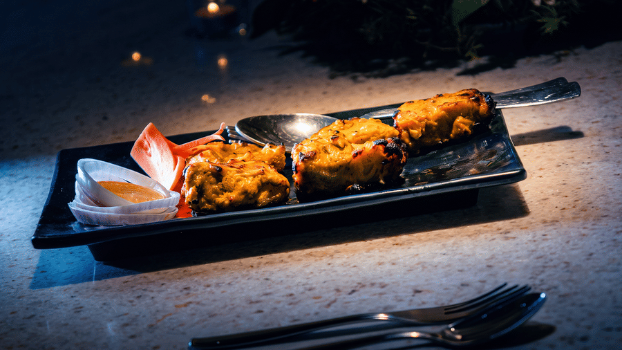 Three tandoor-grilled kebabs with onion slices, a dipping sauce and carved carrot garnish, served by candlelight at Tandoori Tamashaa, Ilara Hotels & Spa, Tada.