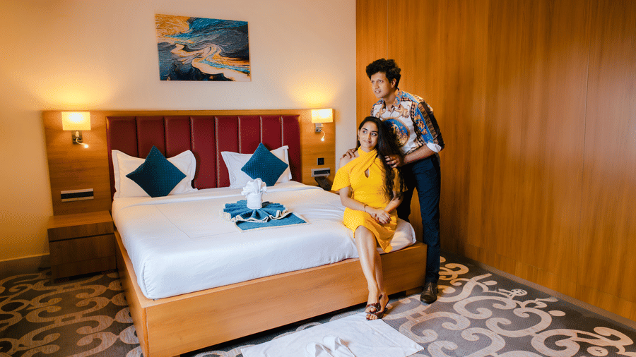 Couple standing beside the Executive Suite king bed with red headboard, teal cushions, bedside lamps and abstract wall art at Ilara Hotels & Spa, Tada.