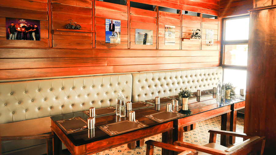 A restaurant dining area featuring wooden panelled walls, a long cushioned bench, and wooden tables and chairs | Vintage Trails By Ilara