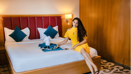 Guest seated on the king bed of the Executive Suite, which has a red panelled headboard, teal cushions and a folded towel design at Ilara Hotels & Spa, Tada.