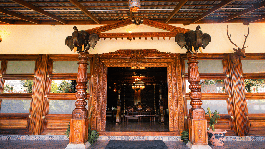 A daytime view of a traditional wooden building entrance featuring carved wooden pillars and panels | Vintage Trails By Ilara