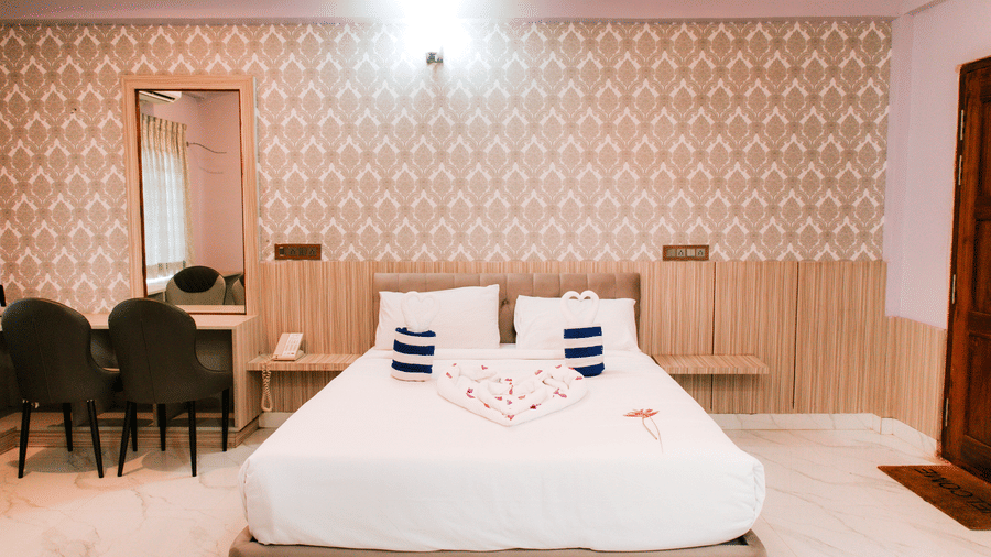 A well-lit bedroom showing a double bed, a dressing table with 2 dark chairs, and patterned wallpaper | Vintage Trails By Ilara