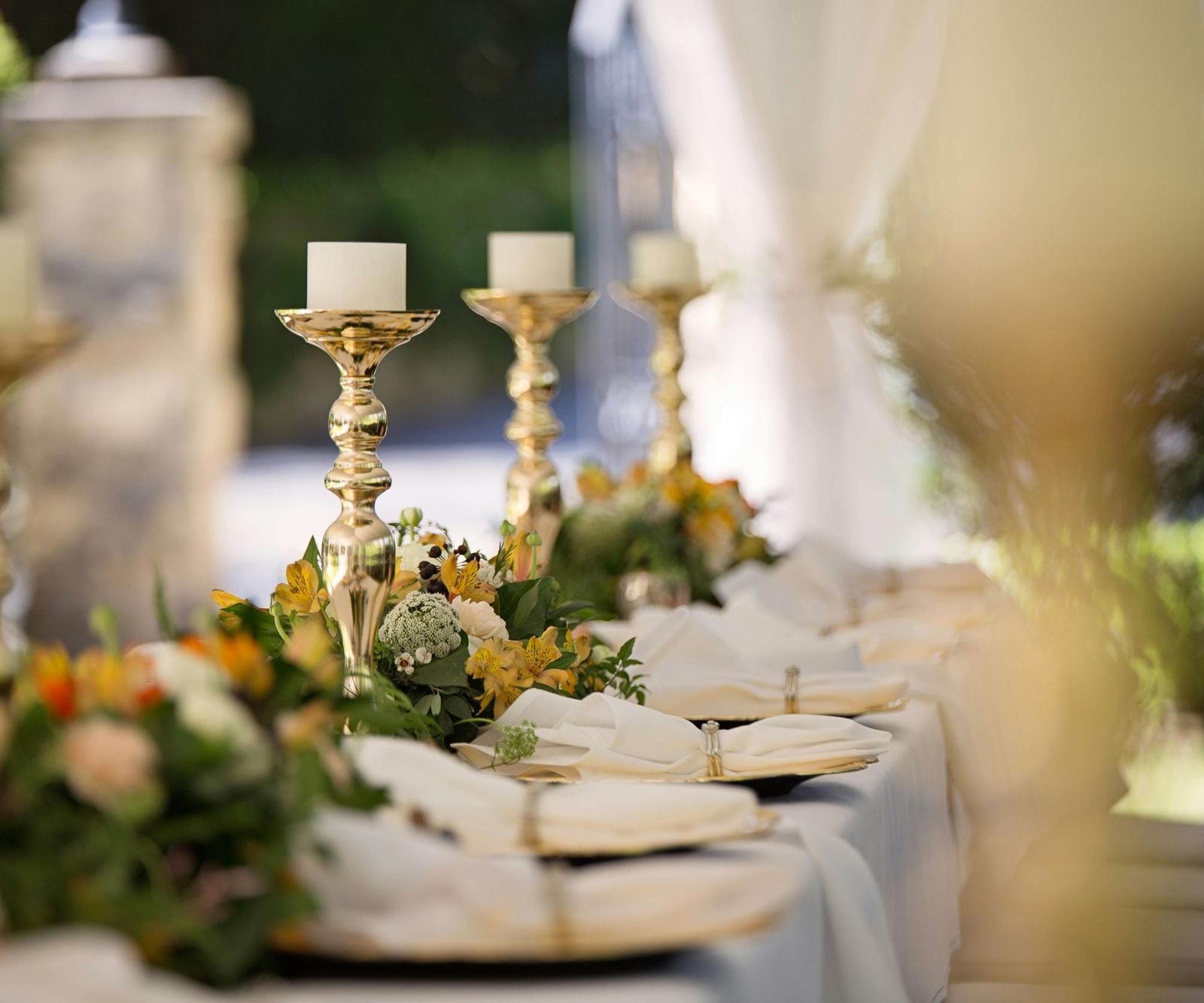 A long table covered with a table cloth decorated with shinny candle stands and well-arranged cutlery.