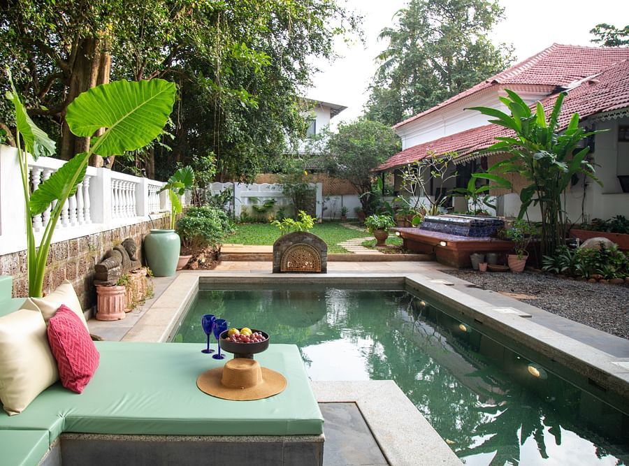 alt-text An image of a plunge pool with a seating arrangments on the side of the pool surrounded by trees and plants at Lamrin Ucassaim Hotel, Goa