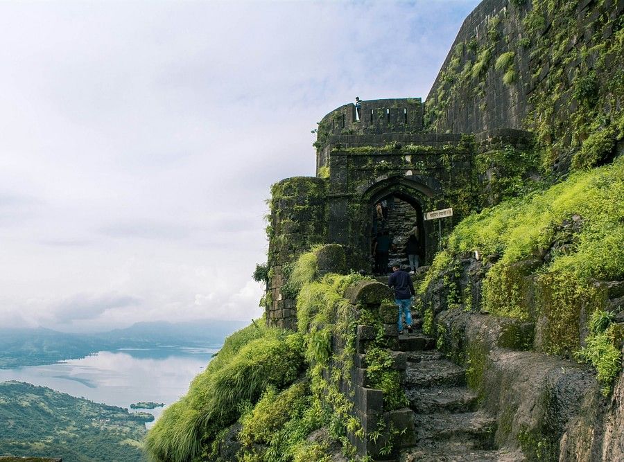 Ancient stone steps and archways covered with green moss on a foggy mountain, evoking a sense of mystery and historical depth in a natural setting.
