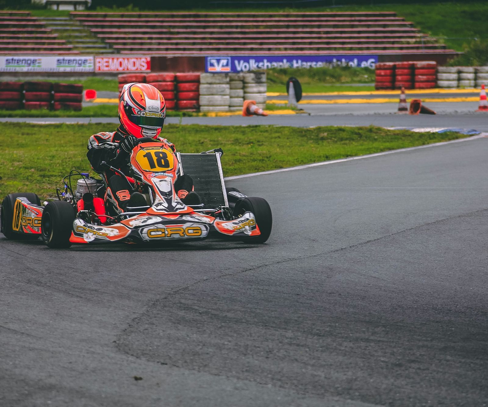 A person driving a go-kart on a race track with seating area in the background