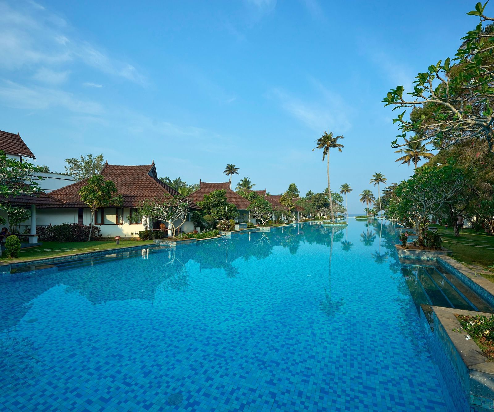 india's largest swimming pool with rooms on one side and trees on another - Rhythm Kumarakom