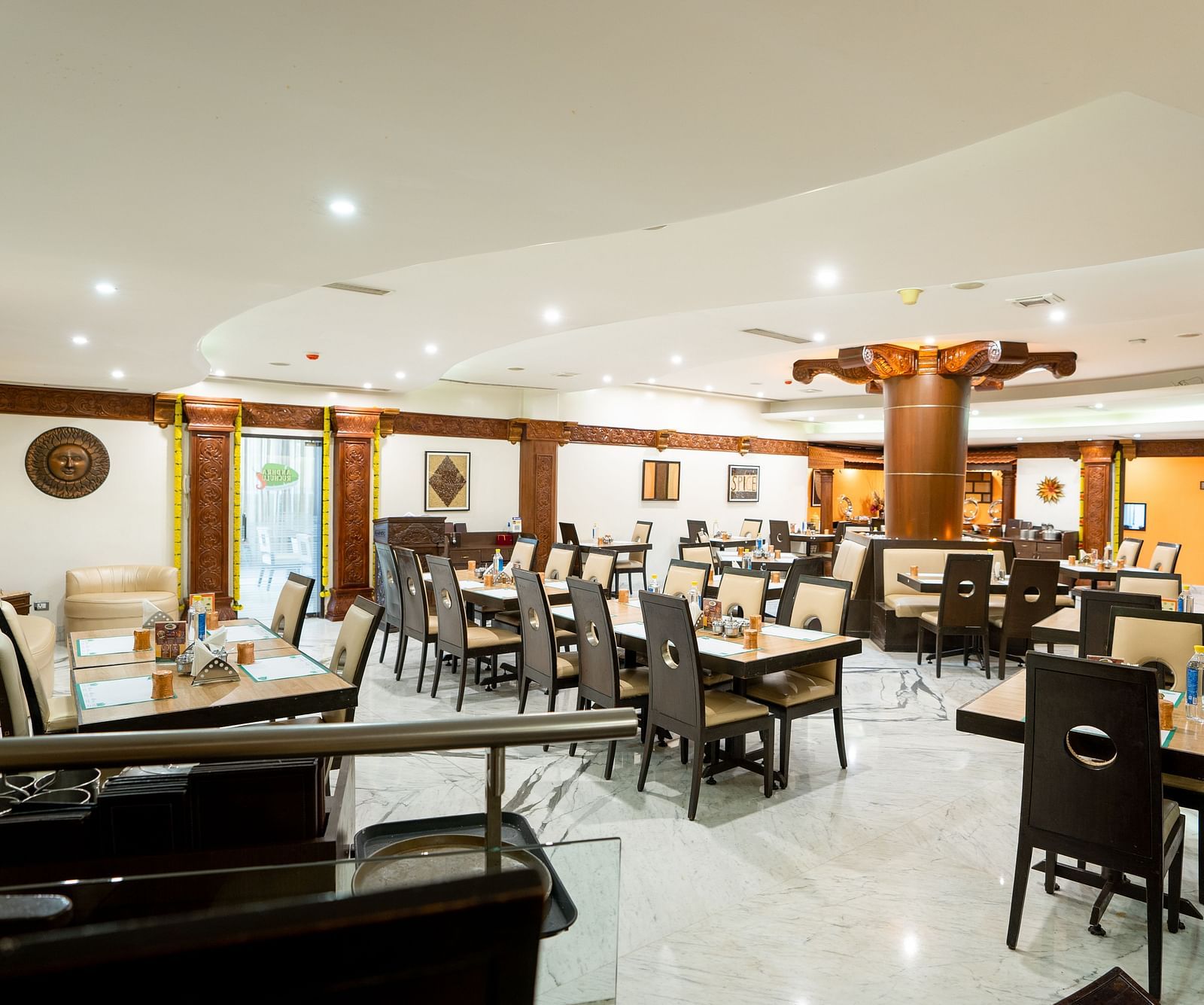 A spacious and well-lit restaurant interior with neatly arranged tables and chairs set for dining under a warm ambient lighting - The President Hotel Jayanagar, Bangalore