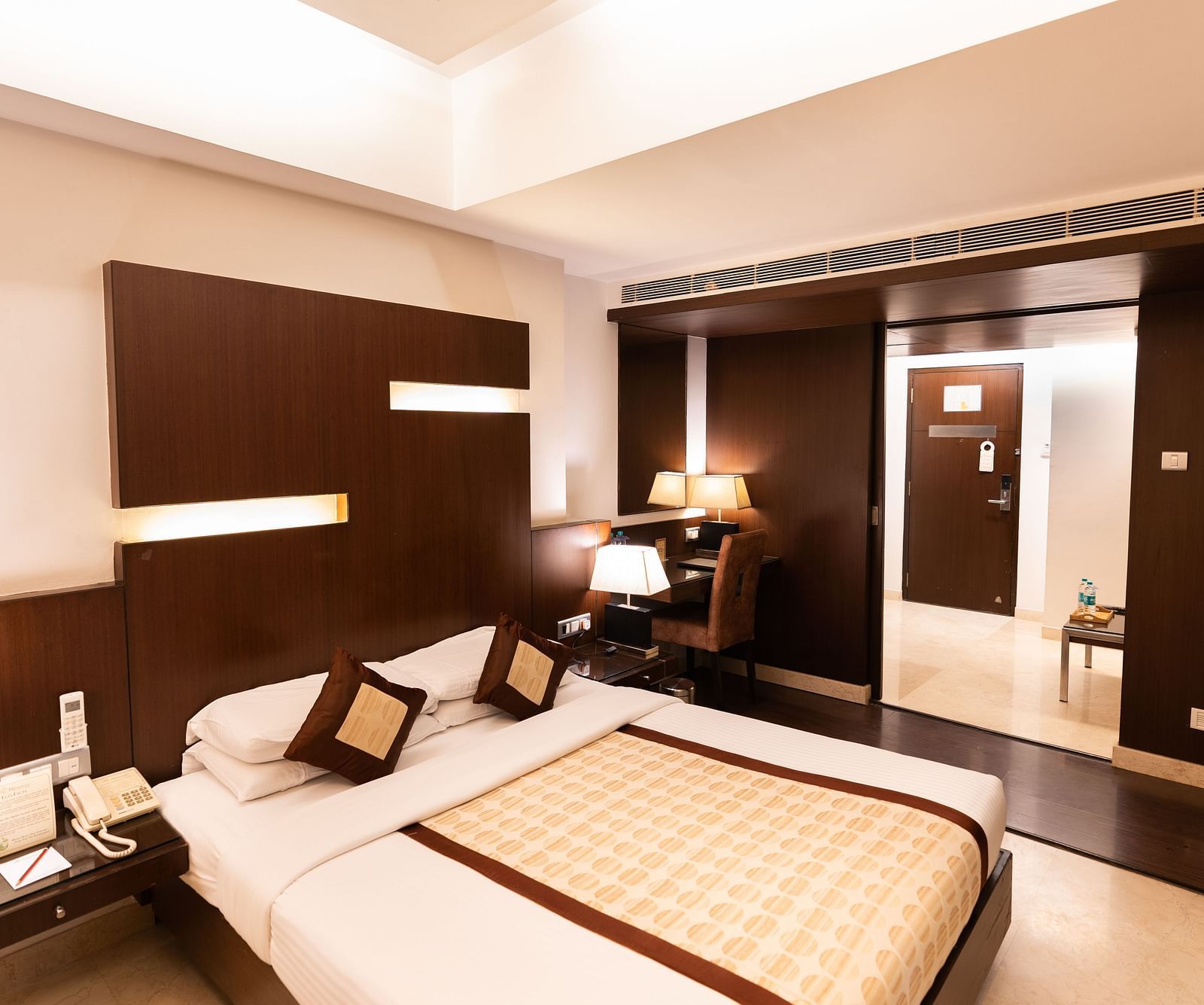 A modern hotel room featuring a large bed with brown headboard, sleek furnishings, and ambient lighting for a comfortable stay - The President Hotel Jayanagar, Bangalore