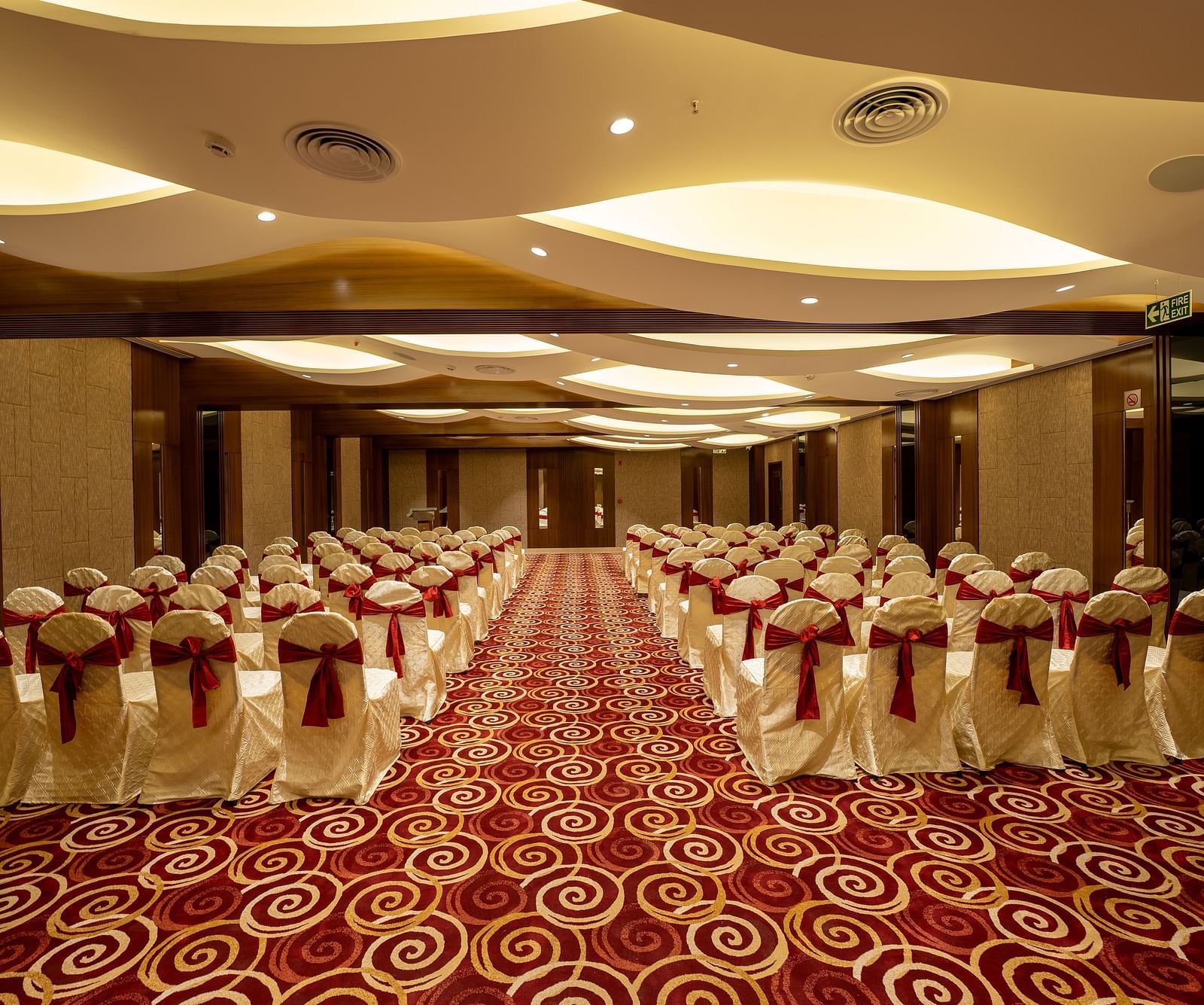 An image of a banquet hall set for an event with chairs draped in white covers and a red-and-white patterned carpet - The President Hotel, Kumara Park, Bangalore