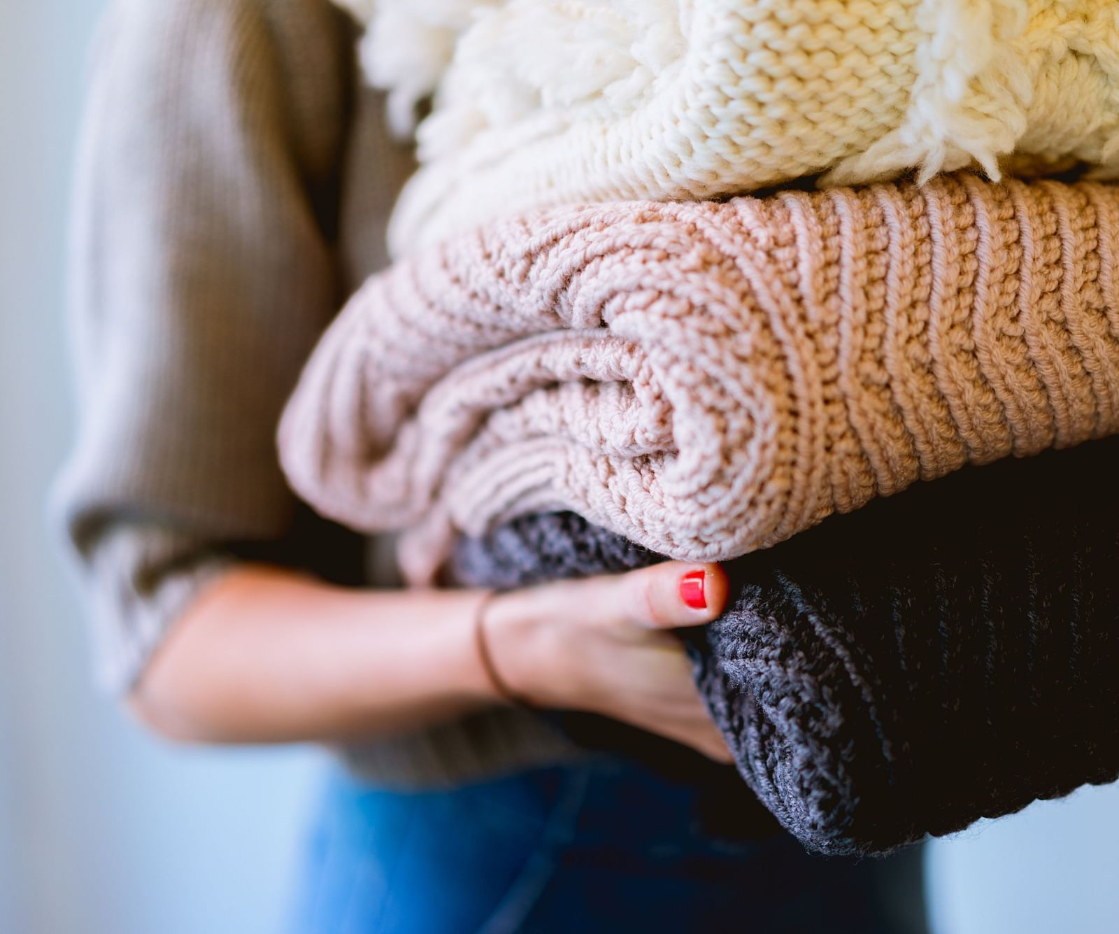 An image of a person holding a stack of folded knitted blankets.