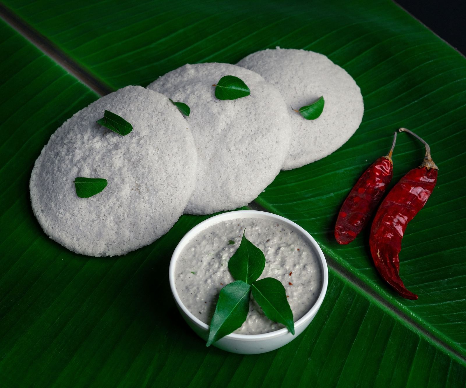 An image of idli with coconut chutney and two red chillies beside it.