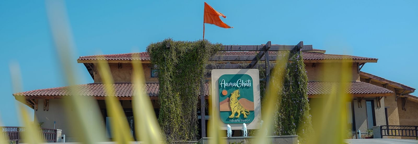 The grand main entrance of the resort under a clear blue sky, with a flag, at Aamaghati Wildlife Resort.