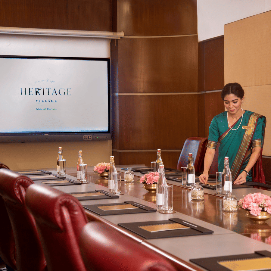 Conference room with a staff member arranging items on the table at Heritage Village Resorts & Spa, Manesar.