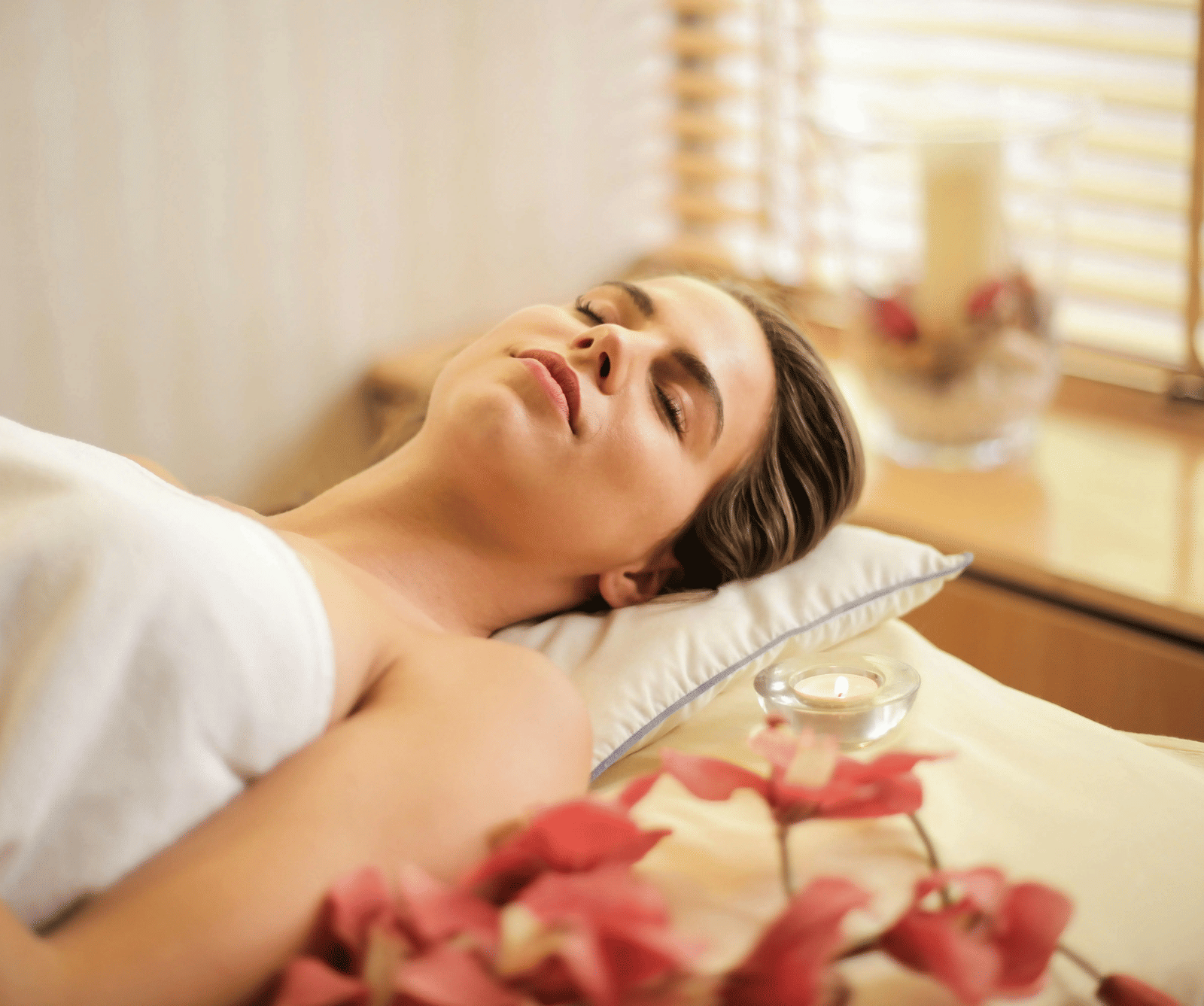 A woman lying down on a bed all relaxed in a brightly lit room.