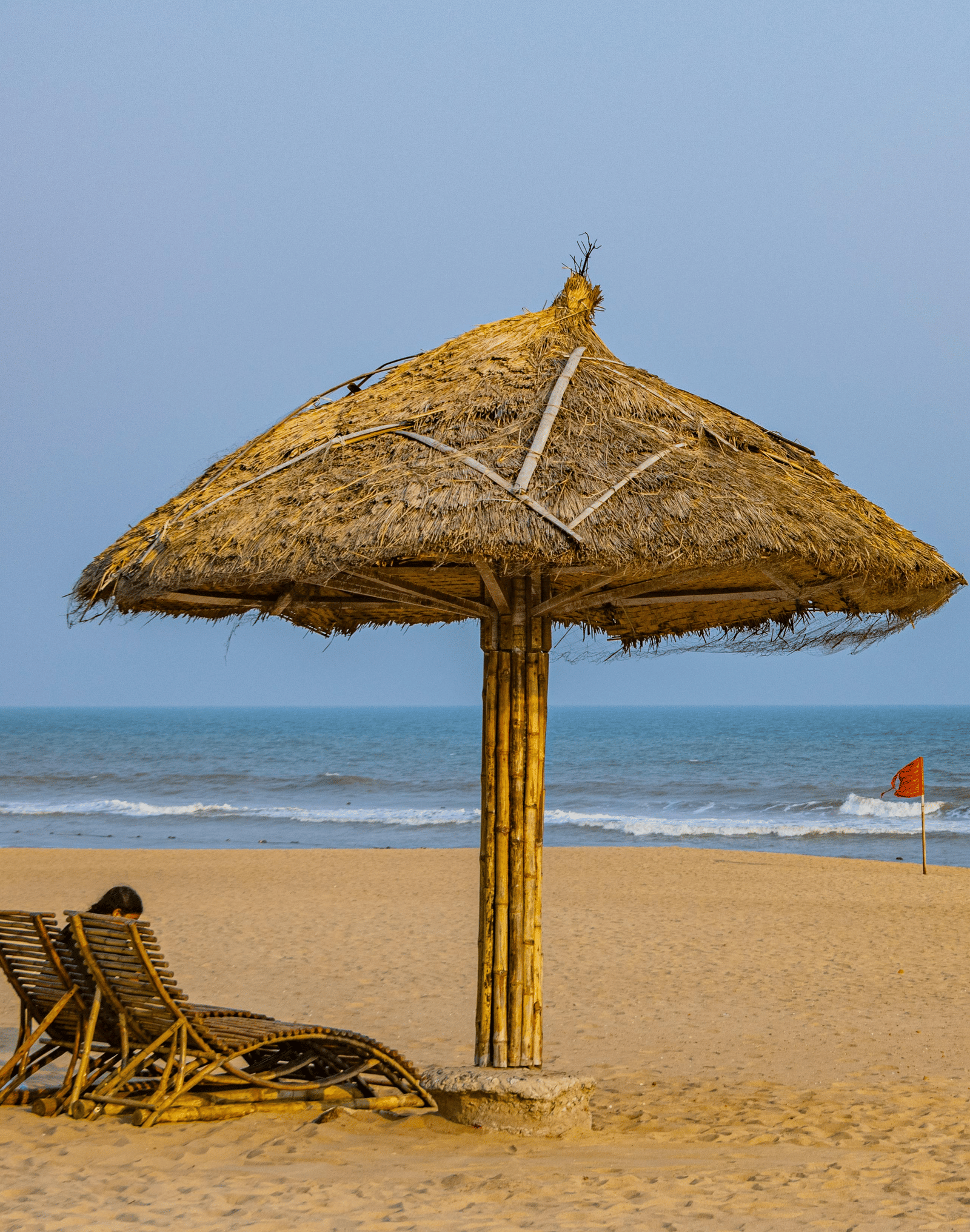 Straw umbrella and wooden chairs placed on a sandy beach near the water.