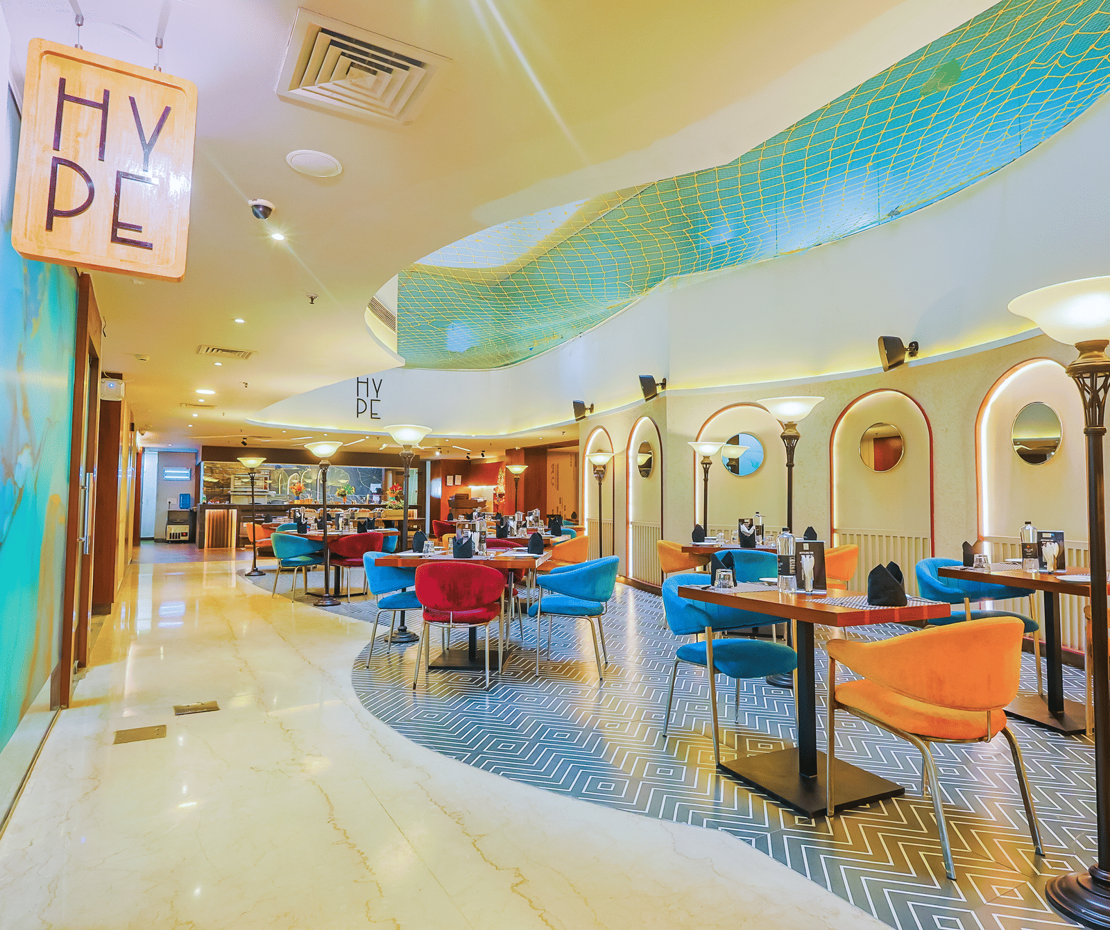 A contemporary restaurant or cafe interior with colourful seating, varied table sizes, and bright lighting, creating an inviting atmosphere.